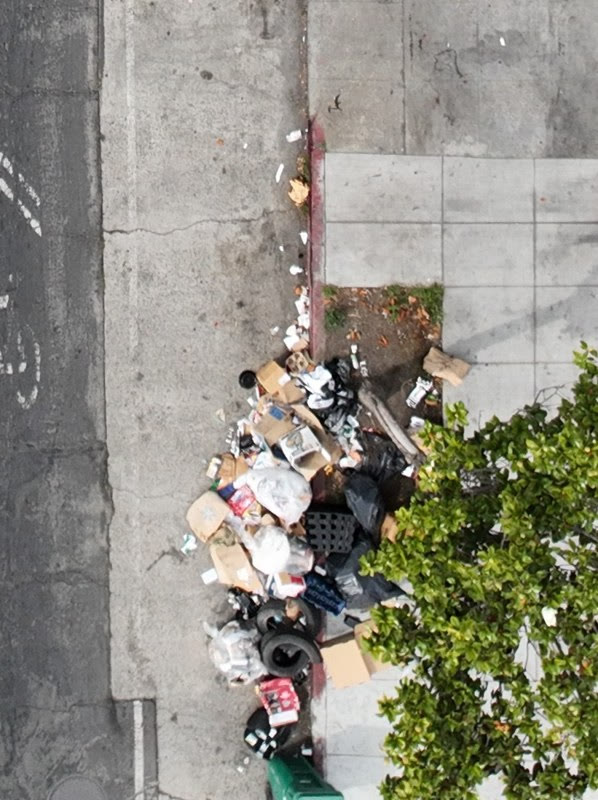 Aerial view of an illegal dumping pile on a sidewalk next to a parked car