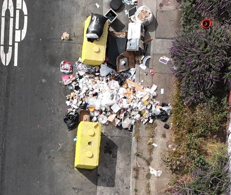Aerial view of an illegal dumping pile beside a yellow dumpster